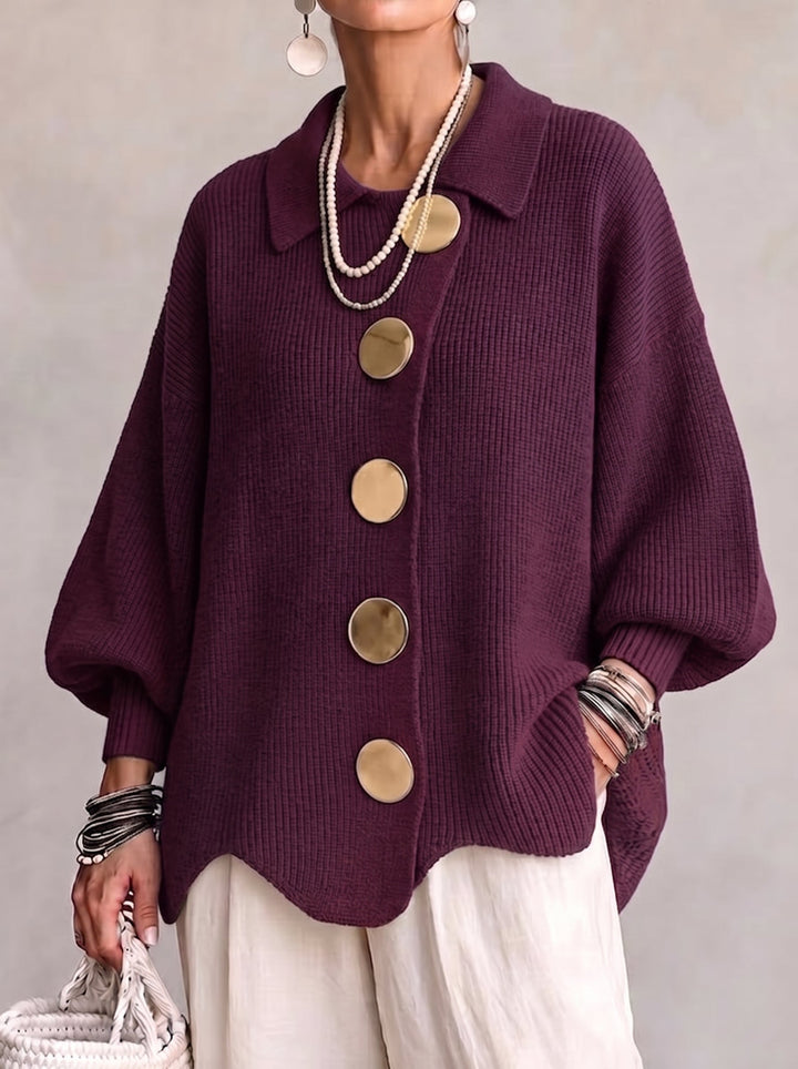 Model i blommefarvet ribstrikket cardigan med spids krave og store guldfarvede knapper, set forfra med hvide bukser. 2