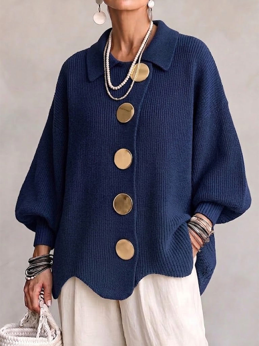 Model i marineblå ribstrikket cardigan med store guldfarvede knapper og bølgekant, båret med hvide bukser og perlekæder. 1