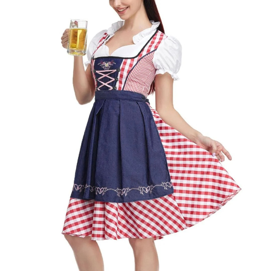 Model i dirndl med marineblåt forklæde og rød-hvid tern, der holder et glas øl og lader skørtet svinge. 2