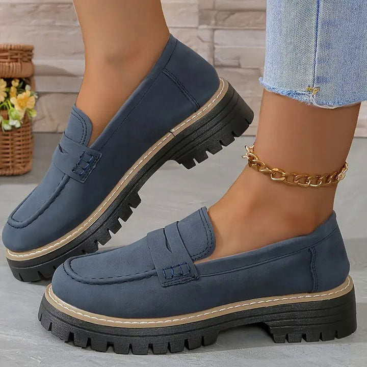 Marineblå ruskindslignende loafers med tyk sort sål og beige kant, båret med guldfarvet ankelkæde og flosset jeans. 16