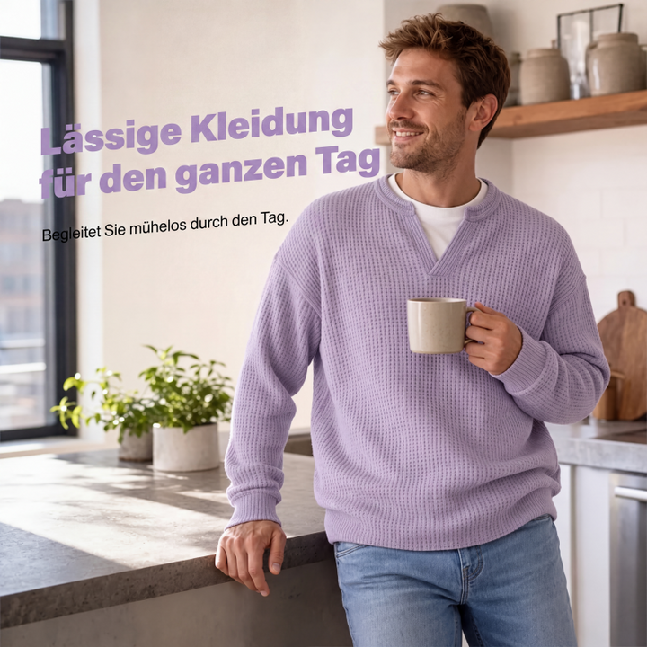 Smilende mand i lilla vaffelstrik læner sig mod køkkenbordet med en kop kaffe i hånden. 5