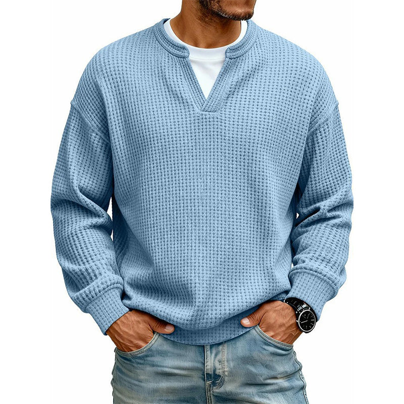 Mand i lyseblå vaffelstrikket top med V-udskæring over hvid T-shirt, hænder i lommerne på jeans. 12