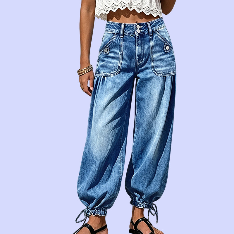 Nærbillede forfra af blå tøndejeans med høj talje, knaplukning, store lommer og bindebånd ved sømmen på lilla baggrund. 10