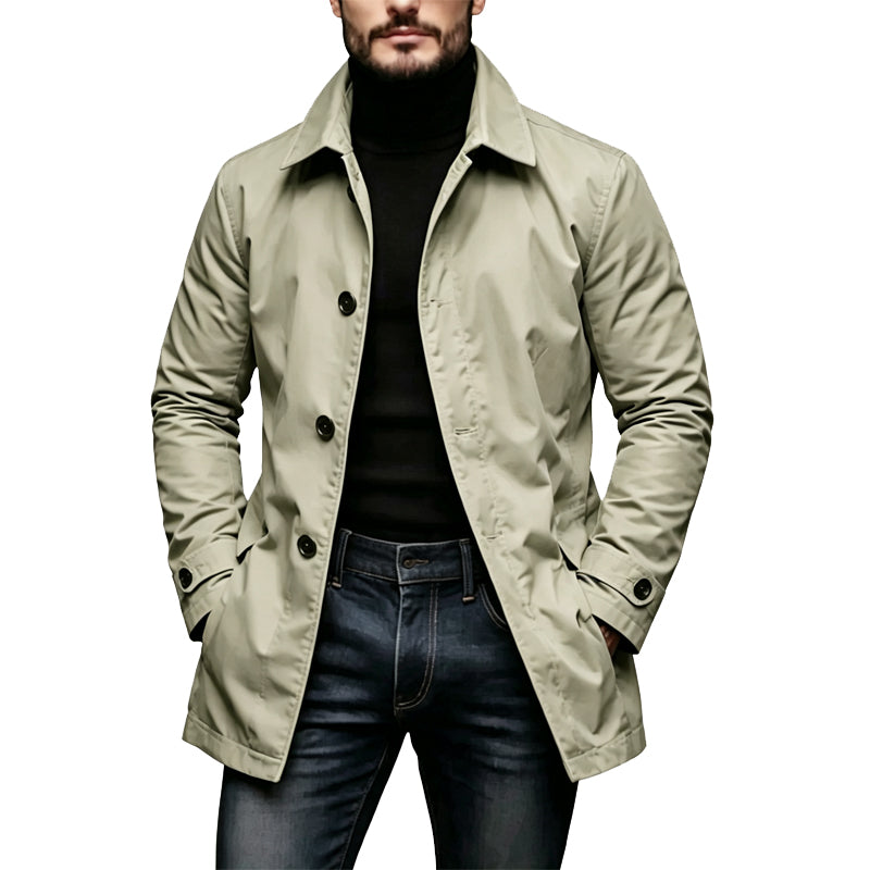 Mand i lys beige-grøn mellemlang trenchcoat med sorte knapper, båret over sort rullekravetrøje og mørkeblå jeans. 3