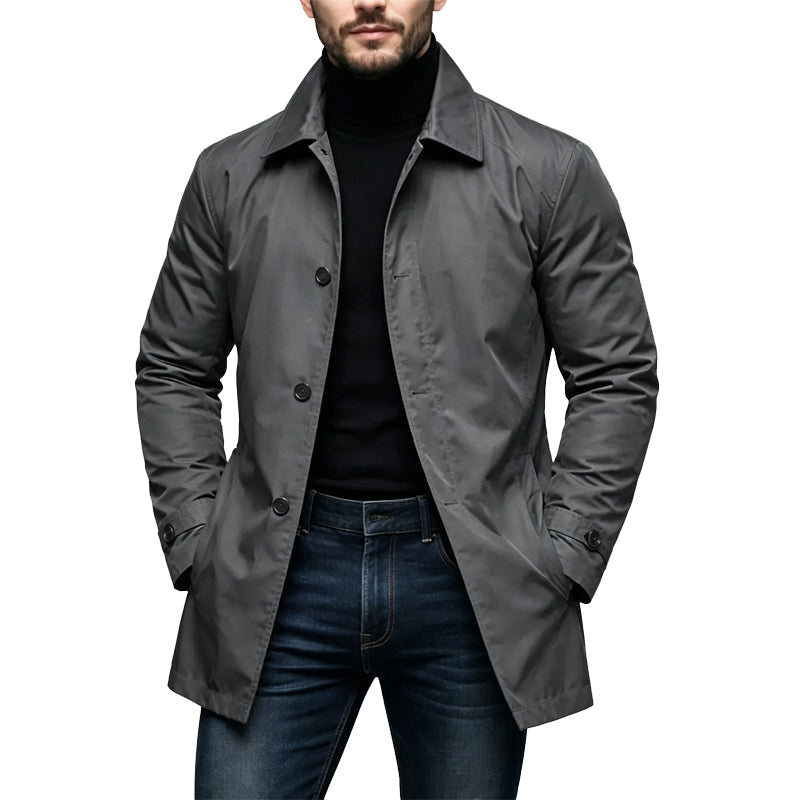Mand i grå mellemlang trenchcoat med knaplukning og skjult lukning, båret over sort rullekravetrøje og mørke jeans. 2