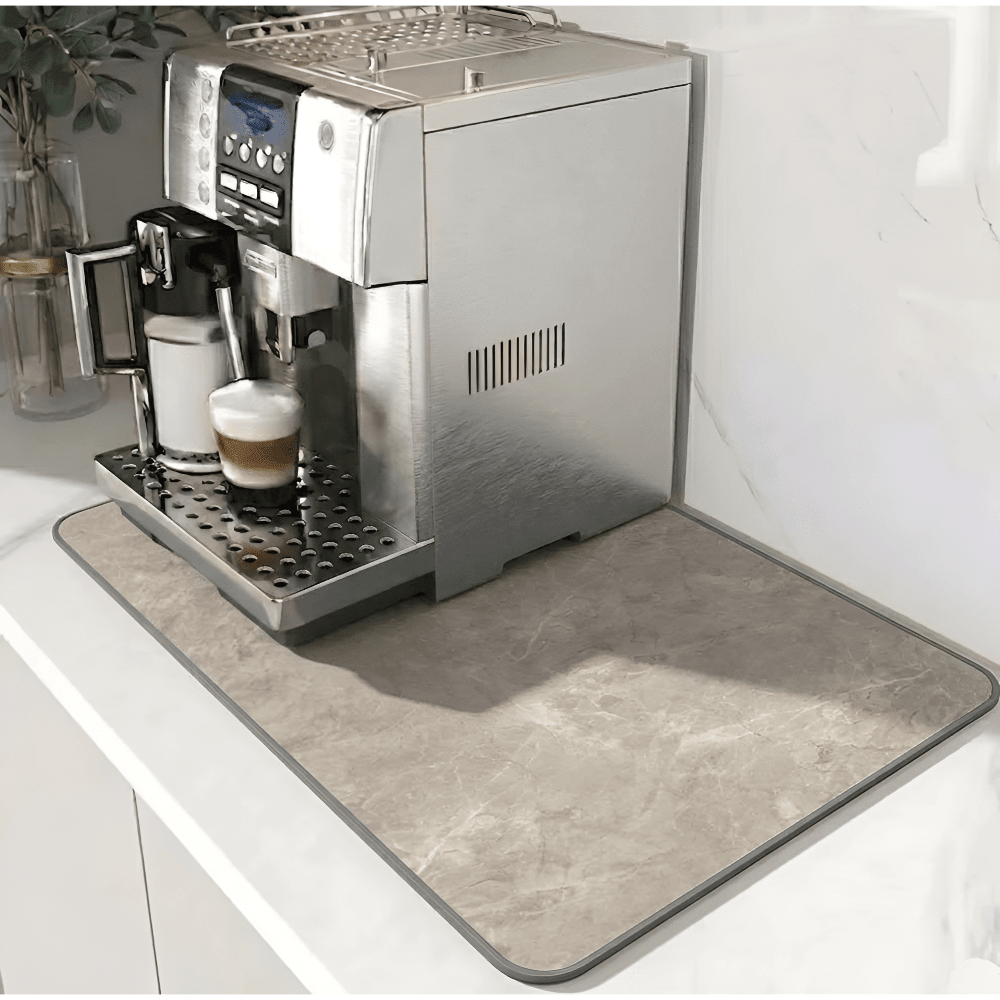 Beige måtte med stenmønster og grå kant under en kaffemaskine på en hvid bordplade. 11
