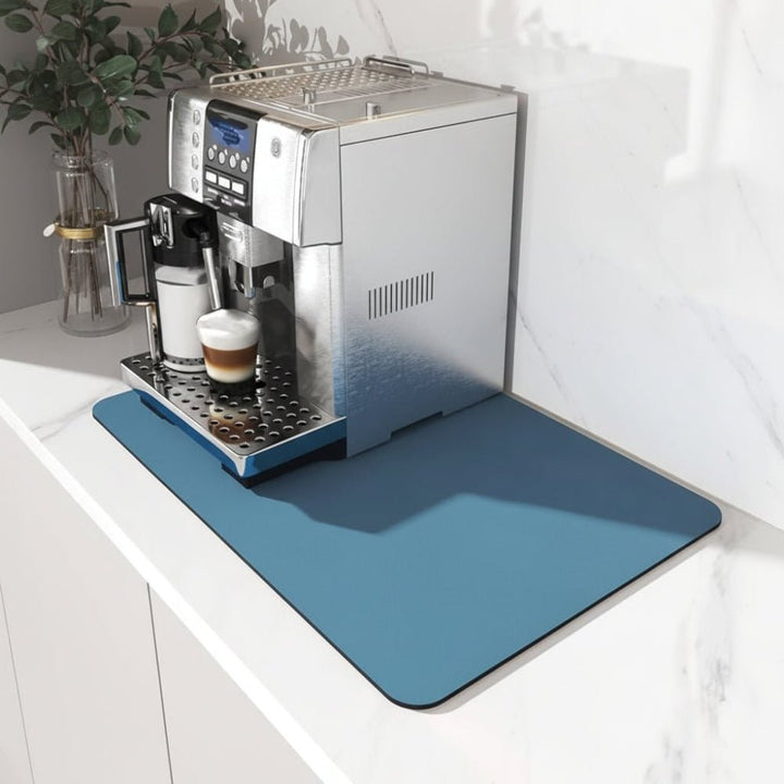 Blå rektangulær måtte med afrundede hjørner under en espressomaskine på en hvid marmorbordplade, set skråt fra siden. 1