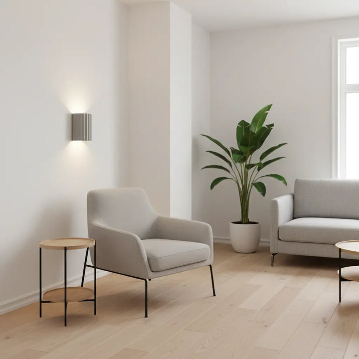 Lysegrå væglampe på hvid væg i stue med lænestol, sofa og stor grøn plante 5