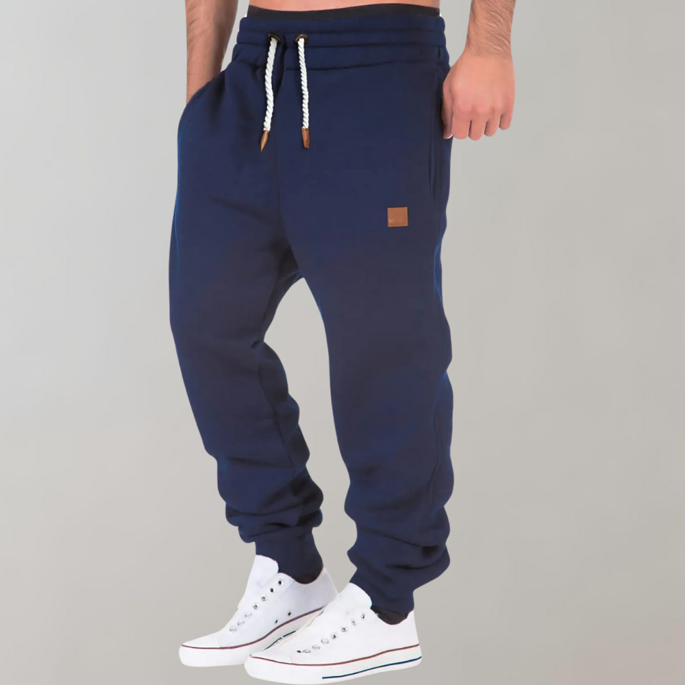 Model i marineblå joggingbukser med hånden i lommen, set lidt fra siden med hvide sneakers 5
