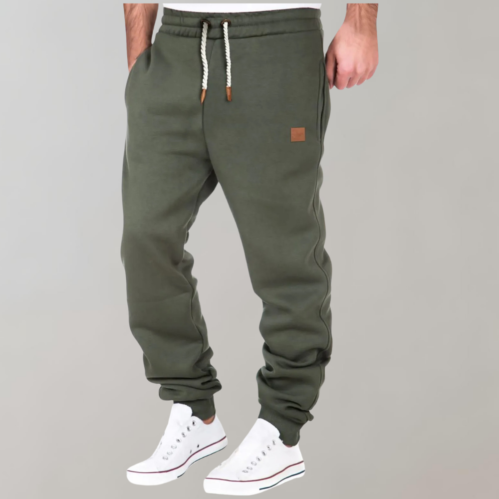 Model i olivengrønne joggingbukser med hånden i lommen og hvide sneakers, set lidt fra siden 3