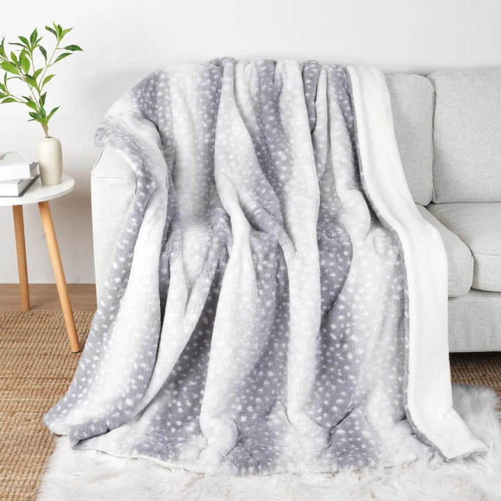 Tæppet i grå og hvid udgave med små hvide pletter, draperet over en lys sofa med hvid fleece på kanten. 7