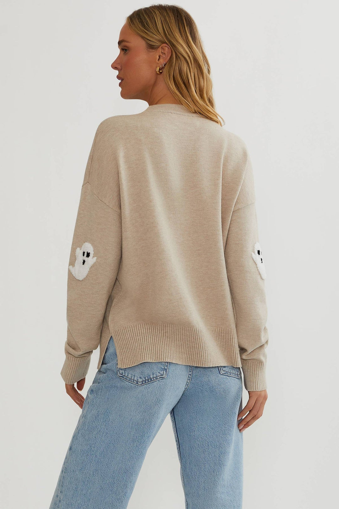 Model set bagfra i beige sweater med glat ryg, spøgelsesapplikationer på ærmerne, slidser i siden og lyse jeans. 5