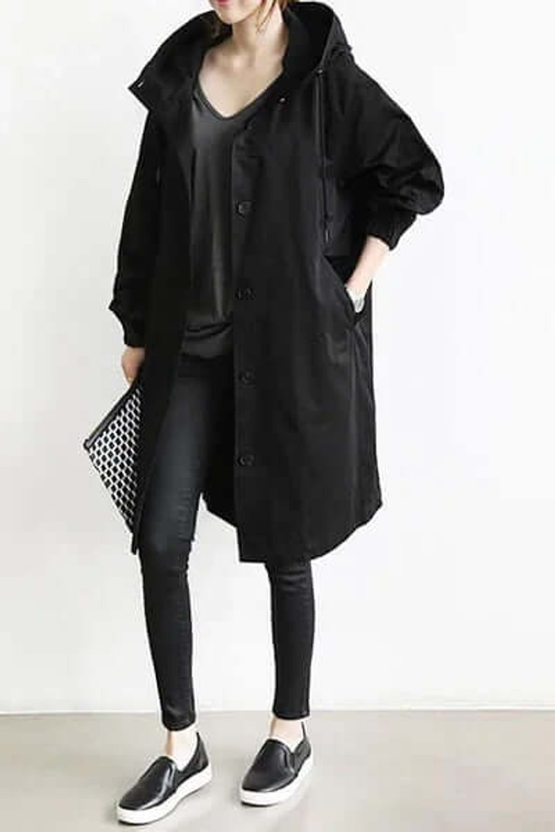 Model i sort trenchcoat med hætte, åben foran, med sorte bukser, sneakers og clutch 3