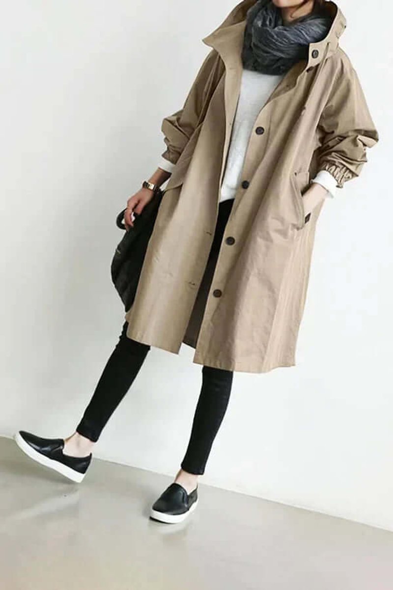 Model i beige trenchcoat med hætte og elastiske ærmeopslag, set på skrå med sorte sko 5