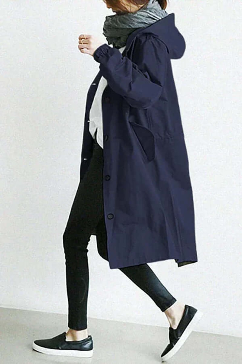 Model i marineblå trenchcoat med hætte set fra siden, gående i sorte sneakers 8